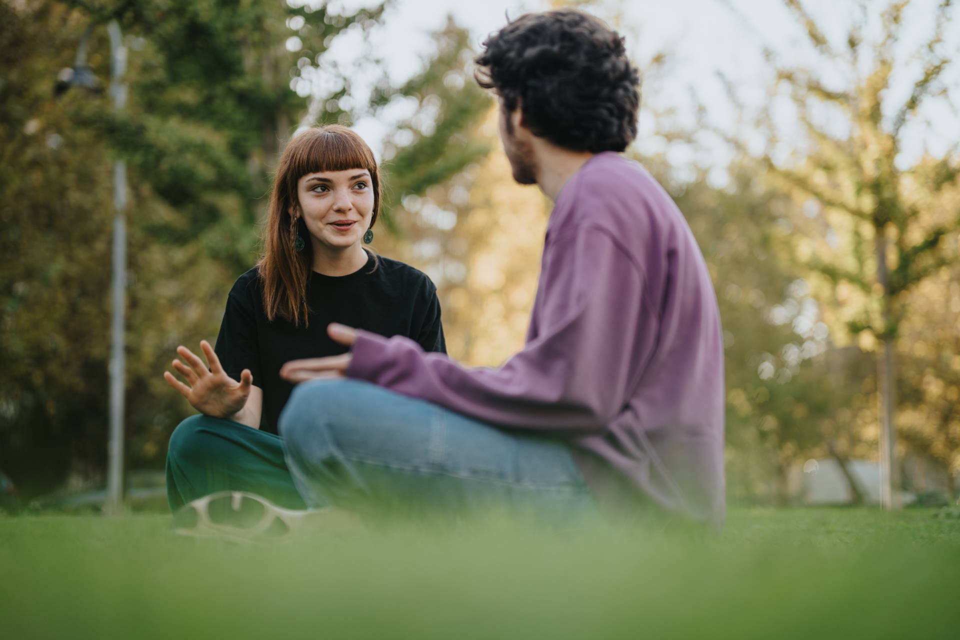 Zwei junge Personen sitzen auf einer Wiese und unterhalten sich freundlich